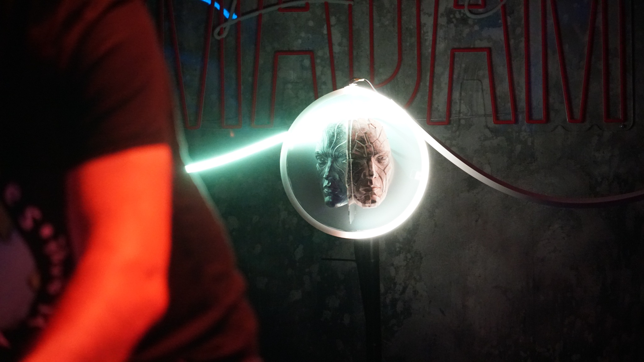 Silent Sentinel installed in a dark venue, with a visitor in the foreground and the illuminated sculpture against a concrete wall